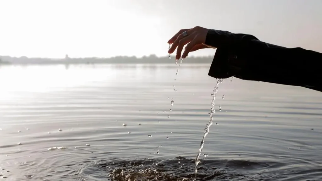 Hand drips water into a serene lake at sunrise, symbolizing prayer for forgiveness and letting go